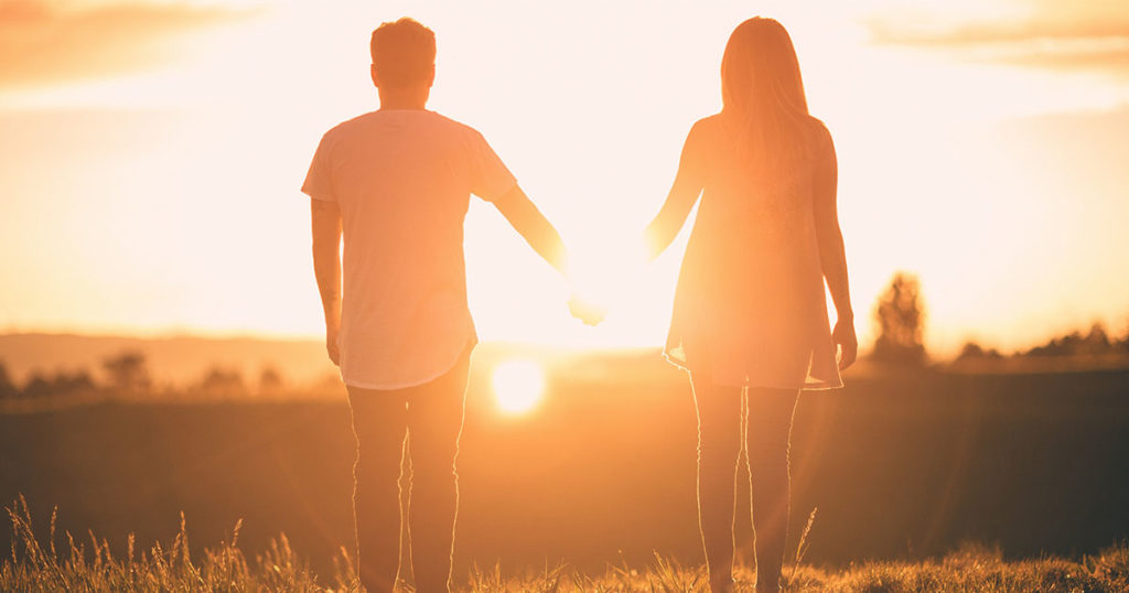 Photo of a man and a woman holding hands with the sun setting in the background.